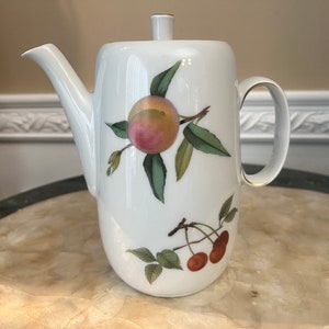 Peut inclure: Théière en porcelaine blanche avec un bord doré et un motif peint d'une pêche et de cerises sur une branche.