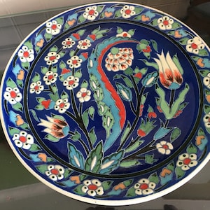 May include: A blue and white ceramic plate with a floral design. The plate features a central motif of stylized tulips and leaves, surrounded by a border of smaller flowers and leaves.