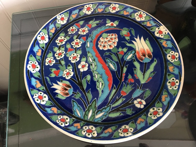 May include: A blue and white ceramic plate with a floral design. The plate features a central motif of stylized tulips and leaves, surrounded by a border of smaller flowers and leaves.
