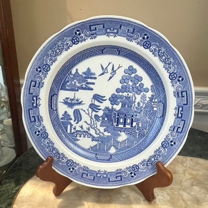 May include: A blue and white porcelain dinner plate featuring a traditional willow pattern design. The plate depicts a central image of a pagoda, a willow tree, and birds. The plate's border is decorated with a repeating pattern of geometric shapes.