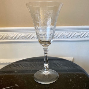 May include: A clear glass wine goblet with a delicate etched design. The goblet has a tall, slender stem and a wide, flared bowl.