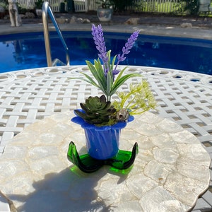 May include: A blue glass planter with a swirl design, holding a succulent and lavender flowers. The planter is sitting on a white mother of pearl tray.