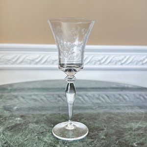 May include: A clear glass wine glass with a delicate etched floral design. The glass has a tall stem and a round base.
