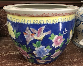 May include: A large blue and white porcelain planter with a yellow rim and floral and bird designs. The planter is decorated with pink, yellow, and green flowers and two birds in flight.