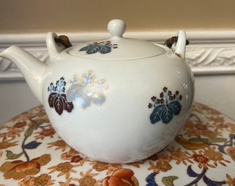 May include: White porcelain teapot with a floral design in shades of blue, red, and gold. The teapot has wooden handles and a lid.