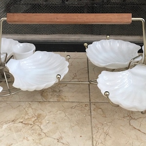 Puede incluir: Un juego de servir de cerámica blanca con un marco de metal plateado y un asa de madera. El juego incluye seis cuencos en forma de concha y un cuenco pequeño redondo.