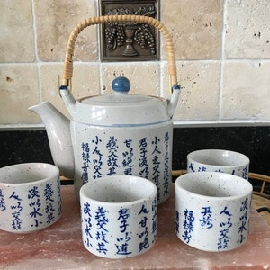 May include: A white ceramic teapot with a bamboo handle and blue and white calligraphy. The teapot is surrounded by four matching teacups with blue and white calligraphy.