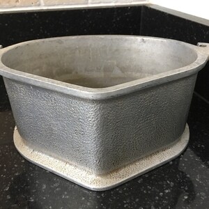 May include: A silver aluminum baking dish with two handles. The dish has a textured surface and a rounded, triangular shape.