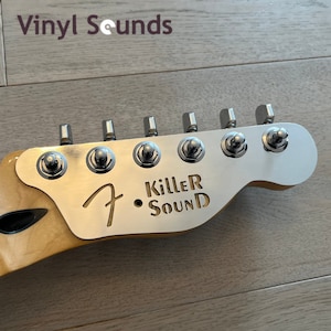 Może przedstawiać: Zbliżenie na srebrny korpus gitary z sześcioma kluczykami i metalową płytką z wygrawerowanym tekstem "Killer Sound".