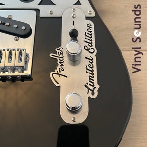 May include: Close-up of a black electric guitar with a silver control plate. The plate has the Fender logo, two knobs, and the text "Limited Edition".