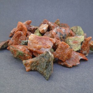 Puede incluir: Un montón de pequeñas piedras rugosas de color rojo, verde y blanco. Las piedras tienen una forma irregular y un aspecto moteado.