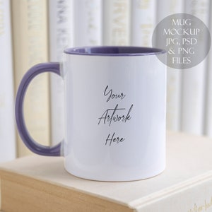 Pode incluir: Caneca de cerâmica branca com borda e alça roxas. A caneca está em cima de uma pilha de livros. O texto "Your Artwork Here" está impresso na caneca.
