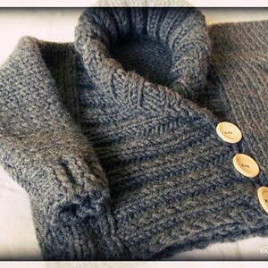 May include: A gray knitted sweater with a large, folded collar and three wooden buttons. The sweater has a textured knit pattern and is likely made of wool or a similar material. The sleeves are visible, and the garment appears to be handmade.