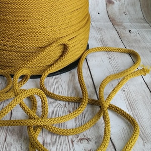 Può includere: Un rotolo di cordoncino giallo senape, con un pezzo di cordoncino disposto su una superficie di legno sbiancato.
