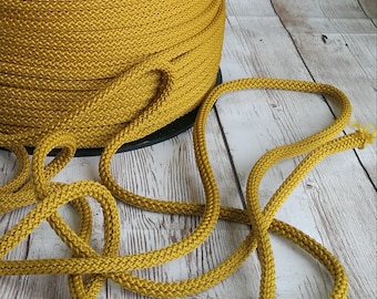 Puede incluir: Una bobina de cordón amarillo mostaza, con un tramo de cordón dispuesto sobre una superficie de madera blanqueada.