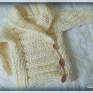 May include: Cream-colored, hand-knitted baby cardigan with a hood. The sweater features a ribbed texture, wooden buttons, and long sleeves. The garment is made of soft yarn, perfect for keeping a baby warm.