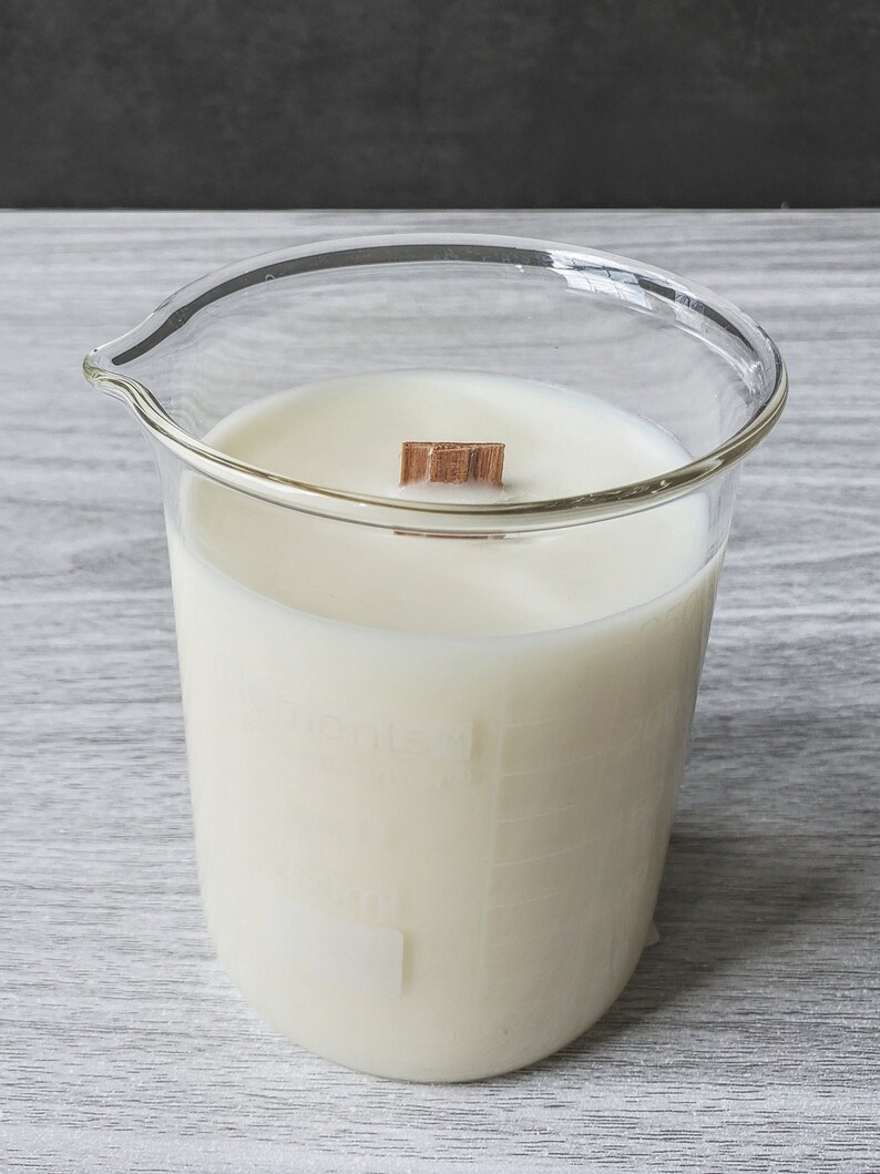 K&ouml;nnte beinhalten: Eine wei&szlig;e Kerze in einem transparenten Glasbecher mit einem Holzdocht. Der Becher hat Messmarkierungen an der Seite. Die Kerze hat ein minimalistisches Design und ist etwa 10 cm hoch.
