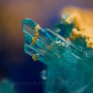 Könnte beinhalten: Nahaufnahme eines blaugrünen Kristalls mit einem daran befestigten gelben Mineral. Der Kristall ist klar und hat eine glasartige Textur.