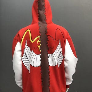 May include: Red hooded sweatshirt with a large graphic on the back featuring a stylized bird or dragon design. The design includes white wings, yellow accents, and a brown spine-like detail. The sleeves are white, and the bottom trim is yellow.