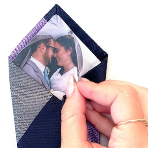 May include: A navy blue and purple patterned tie with a clear plastic pocket containing a wedding photo of a couple.