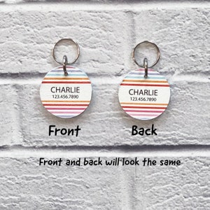 May include: Round, colorful striped dog tag with the name "CHARLIE" and phone number "123.456.7890" printed on it. The tag has a silver metal ring attached to it.