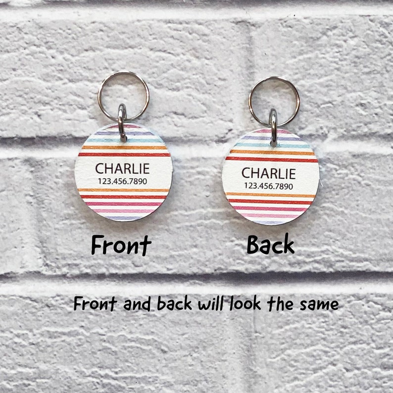 May include: Round, colorful striped dog tag with the name "CHARLIE" and phone number "123.456.7890" printed on it. The tag has a silver metal ring attached to it.