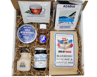 May include: A gift box filled with Maine-themed treats, including wild blueberry tea, blueberry jam, honey, wild blueberry preserves, and a blueberry pancake and waffle mix. The box is filled with brown packing paper.