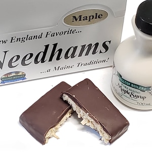 May include: Two Needhams, a Maine tradition, chocolate covered maple pecan candies, broken in half, next to a bottle of Hilltop Boilers Pure Maine Maple Syrup.