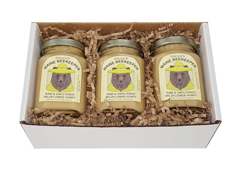 May include: A white box contains three jars of honey. Each jar has a label with a bear wearing a beekeeper hat. The labels read "Maine Beekeeper" and "Raw & Unfiltered Wildflower Honey". Each jar contains 10 oz (283 grams) of honey.