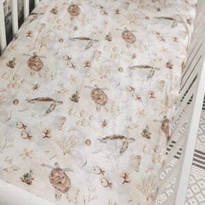 May include: A white crib sheet with a repeating pattern of sea turtles, fish, seahorses, and coral in shades of brown and beige. The sheet is made of soft fabric and is designed to fit a standard crib.