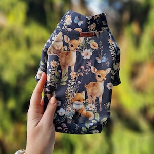 May include: A dark blue dog sweater with a woodland print featuring deer, foxes, and flowers.