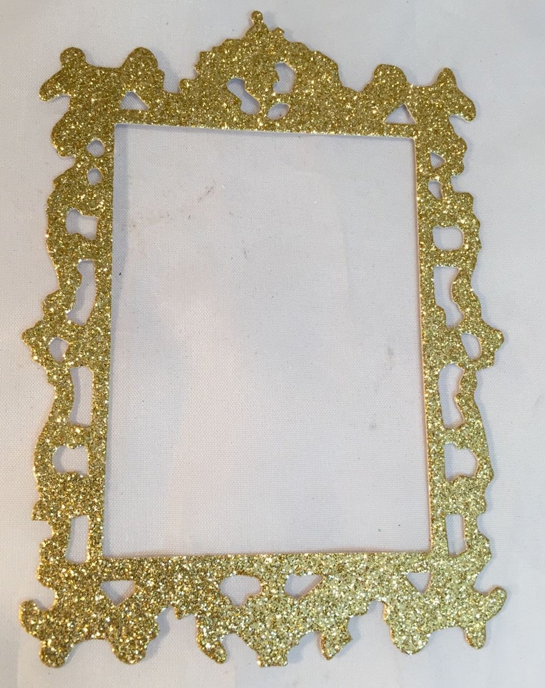 May include: A gold glitter picture frame with an ornate, decorative design. The frame is rectangular with a detailed, textured border. The frame is empty, with a white background visible through the opening.