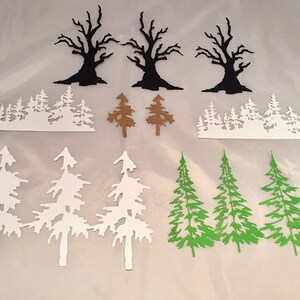 May include: Assortment of paper cutouts featuring trees in various styles. Includes three black bare trees, two brown pine trees, two white forest silhouettes, four white pine trees, and four green pine trees.