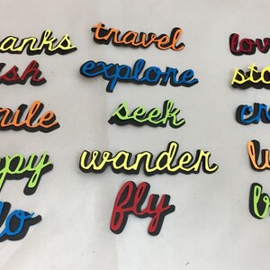 May include: A collection of colorful, die-cut word art pieces. Words include "thanks," "travel," "love," "wish," "explore," "story," "smile," "seek," "create," "happy," "wander," "lucky," "hello," "fly," and "brave." Each word has a black shadow.