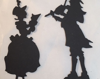 May include: Black silhouette cutouts of two figures. One figure is a person in a dress holding a book, and the other is a person playing a violin. The figures are likely from a historical or theatrical theme.
