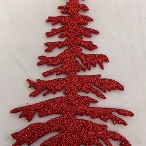 May include: A red glitter Christmas tree decoration. The tree is cut out in the shape of a fir tree with branches and a pointed top. The tree is covered in red glitter and is set against a white background.