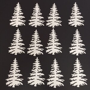 May include: Twelve white paper cut-out evergreen trees arranged on a black background. The trees have detailed branches and a textured appearance, suitable for crafting or holiday decorations.