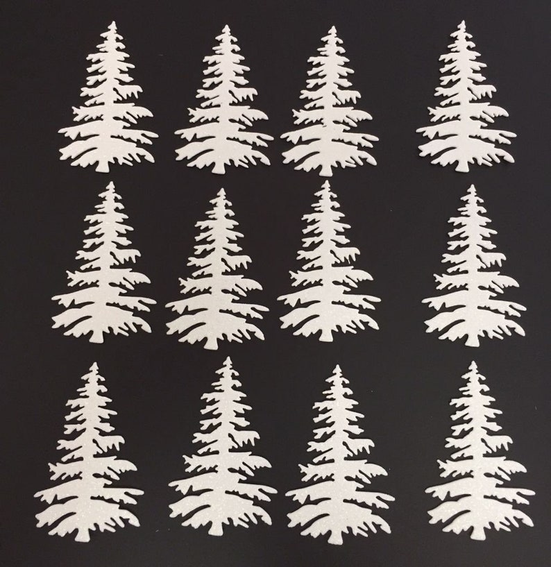 May include: Twelve white paper cut-out evergreen trees arranged on a black background. The trees have detailed branches and a textured appearance, suitable for crafting or holiday decorations.