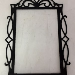 May include: Black decorative frame with an ornate, openwork design. The frame has a rectangular shape with a detailed, symmetrical pattern around the edges and a decorative top. The frame is made of a solid, dark material.