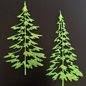 May include: Two glittery green Christmas tree cutouts on a black background. The trees have a detailed, open design with visible branches and a sparkling texture. The trees are similar in shape, perfect for holiday crafts.