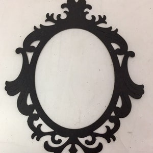 May include: A black, ornate oval frame with a decorative, scroll-like design. The frame has a detailed, symmetrical pattern around the oval opening. The frame is made of a solid, dark material.