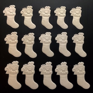 May include: A collection of off-white Christmas stocking-shaped ornaments. Each ornament features a teddy bear and gift design. The stockings have snowflake details and are arranged on a black background. Ideal for holiday crafts and decorations.