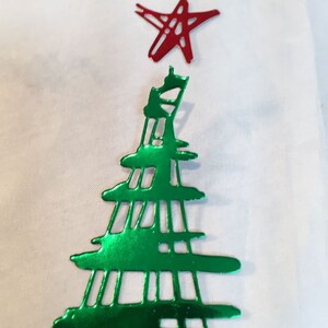 May include: A metallic green Christmas tree ornament with a red star on top. The tree has a cut-out design and is set against a white background. The star is also a cut-out design.