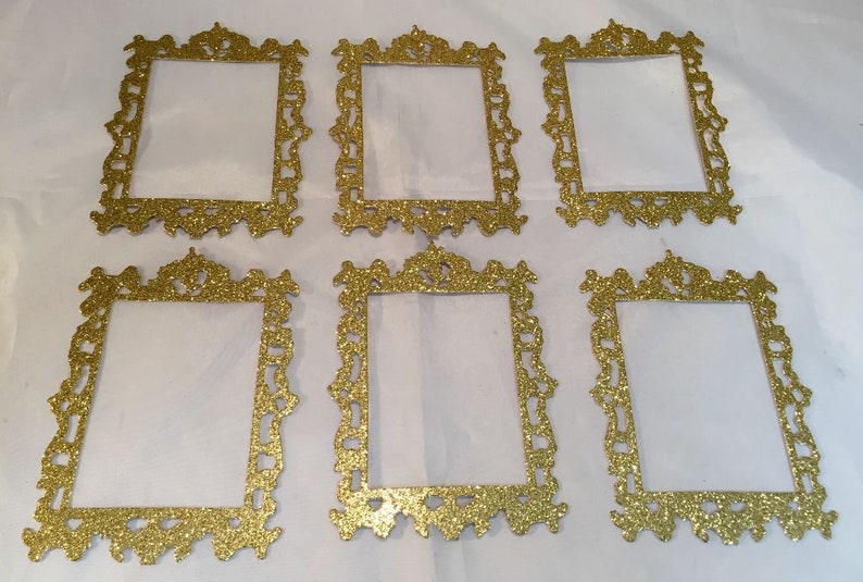 May include: Six ornate, gold glitter picture frames with intricate scrollwork. The frames are rectangular with a blank center, perfect for displaying photos or artwork. The frames are arranged on a white surface.