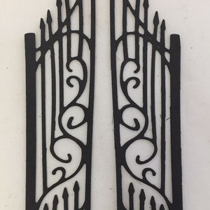 May include: Two black metal decorative gate panels. Each panel features vertical bars, decorative swirls, and pointed finials. The gates are designed with a gothic or Victorian aesthetic, suitable for crafting or decorative projects.