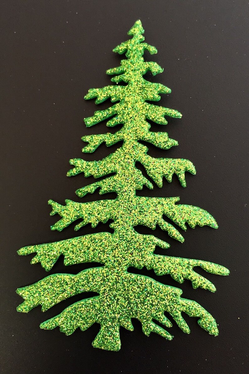 May include: A glittery green Christmas tree-shaped decoration. The tree has a classic evergreen shape with detailed branches and is covered in sparkling green and yellow glitter. The background is a solid black.