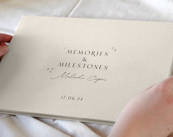 Könnte beinhalten: Ein weißes, mit Leinen bezogenes Fotoalbum mit dem Text "Memories & Milestones" und dem Namen "Malachi Capri" in Kursivschrift. Das Datum "17.06.24" ist unter dem Namen gedruckt.