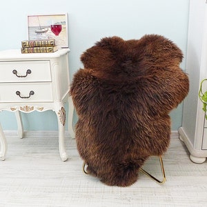 May include: A brown sheepskin rug with long, soft fur. The rug is folded in half and is sitting on a white wooden floor.