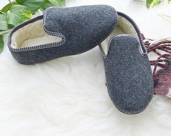 May include: A pair of gray wool slippers with a white fleece lining. The slippers have a simple design with a stitched seam around the edge.