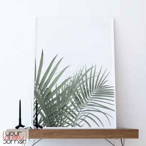 May include: A white framed print of a green palm leaf on a white background. The print is sitting on a wooden shelf with two black candle holders.